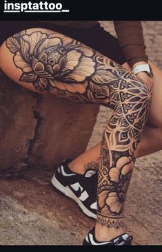 a woman sitting on top of a rock next to a wall with tattoos on her legs