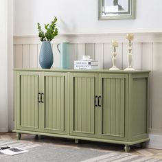 a green cabinet with two doors and some vases on top of it next to a rug