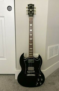 a black electric guitar sitting on the floor next to a white door and carpeted area