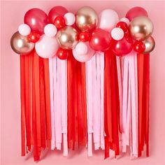 red, white and gold balloons with tassels are hanging on a pink wall