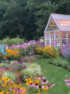 a garden filled with lots of flowers next to a small wooden house on top of a lush green field