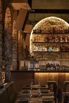 a dimly lit restaurant with wooden tables and chairs, bottles on the wall behind the bar