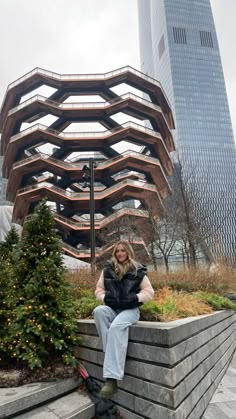 a woman sitting on top of a stone wall next to a tree and tall buildings