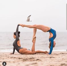 two women doing yoga on the beach with seagulls in the sky behind them