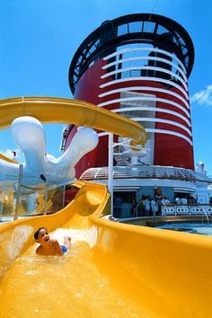 a yellow water slide in front of a red and white building on a cruise ship