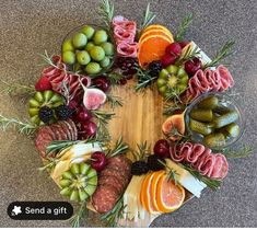 a circular arrangement of assorted fruits and meats on a wooden board with the words send a gift