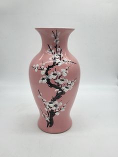 a pink vase with white flowers painted on the front and side, sitting against a white background