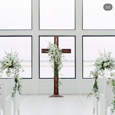 a cross with flowers and greenery on it in front of two windows at the end of a wedding ceremony