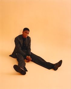 a man sitting on the ground with his legs crossed, wearing striped suit and black shoes