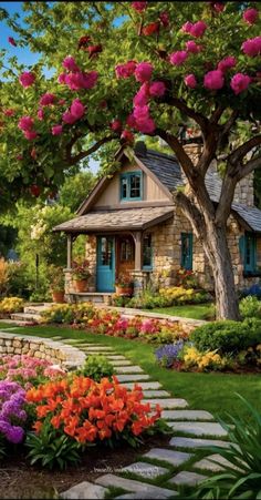 a garden with flowers and trees in front of a small house that is surrounded by stone steps