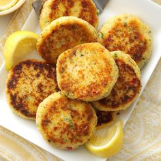 several crab cakes on a white plate with lemon wedges