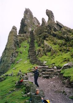 some people are climbing up the side of a mountain with rocks and grass on it