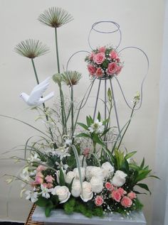 an arrangement of flowers in a basket on a table next to a white dove statue