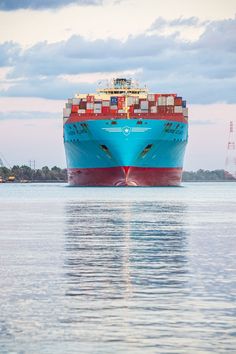 a large blue and red cargo ship in the middle of the ocean under cloudy skies