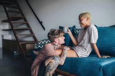 a man sitting on top of a blue couch next to a little boy with tattoos