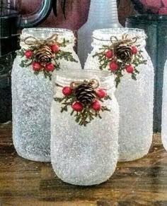 three mason jars decorated with pine cones, holly and red berries are sitting on a table