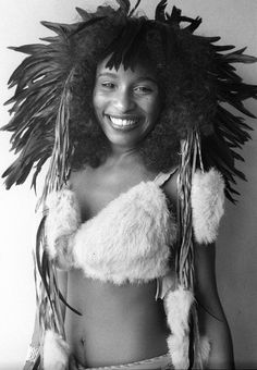 a black and white photo of a woman with feathers on her head wearing a bra