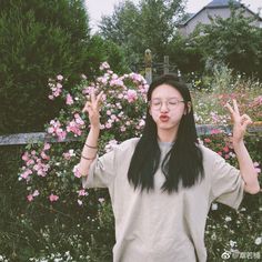 a woman standing in front of flowers holding her hands up to the side with both hands