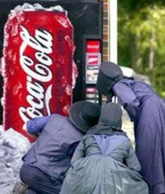 two men are sitting in front of a coca - cola machine with their backs to each other