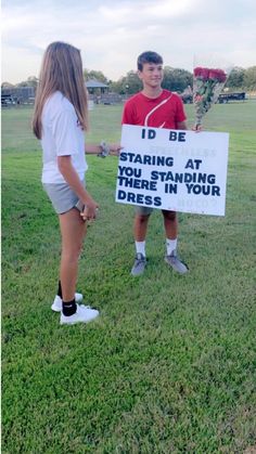 two people standing in the grass with a sign that says i'd be starting at there in your dress