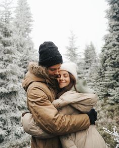 a man and woman hugging in front of snow - covered trees on a cold day