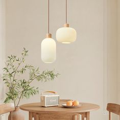 two lights hanging over a wooden table with fruit on it and a plant in the corner