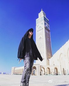 a man standing in front of a tall tower with a clock on it's side