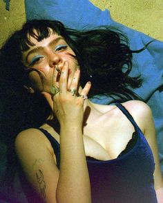 a woman laying on top of a bed with her hands in her mouth and eyes closed