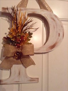 a wooden letter decorated with fall foliage and lights hangs on a door handle in front of a white door