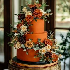 a three tiered orange wedding cake decorated with flowers and greenery on a gold stand