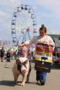 a woman walking with a pig in front of a ferris wheel and fair goers