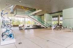 people are sitting at tables in an open space with stairs and glass windows on the wall