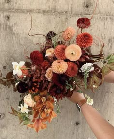 a bouquet of flowers is being held by someone's hand in front of a concrete wall