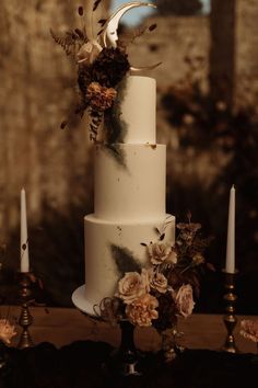 a three tiered white cake with flowers on top and candles in the back ground