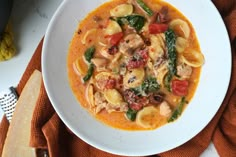 a white bowl filled with pasta and vegetables on top of a red towel next to bread