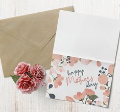 an envelope and flowers on a white wooden table with a card that says happy mother's day