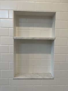 an empty shelf in the corner of a white tiled wall with no one inside it