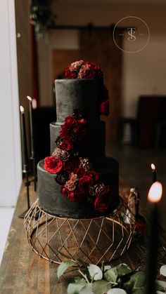 a three tiered wedding cake with red flowers on the side and candles in the background