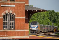 a train traveling down tracks next to a tall brick building with an arched window on the side