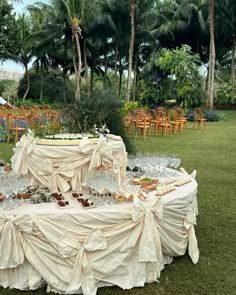 a table covered in white cloths sitting on top of a lush green field next to palm trees