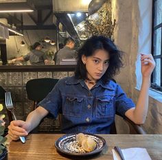 a woman sitting at a table in front of a plate of food with a fork and knife