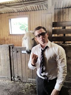 a man wearing glasses and a tie standing next to a white horse in a barn