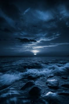 the sun is setting over the ocean with rocks in the foreground and dark clouds above