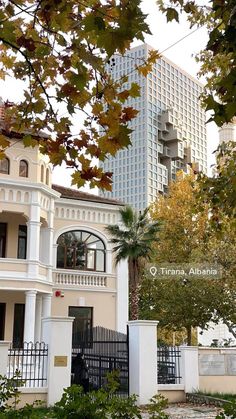 a tall white building sitting next to a lush green forest filled with trees and bushes