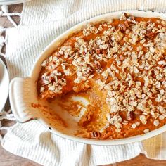 a casserole dish filled with food on top of a white cloth next to two plates