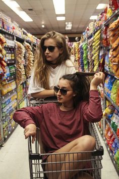 two women sitting in a shopping cart at a grocery store