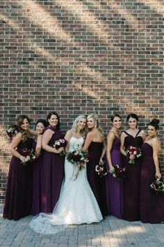 a group of women standing next to each other in front of a brick wall holding bouquets