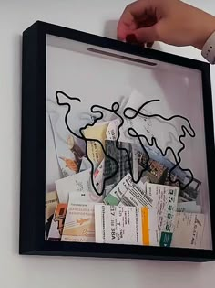 a person holding up a framed artwork with scissors and other items in it's shadow