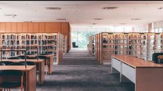 an empty library with rows of bookshelves and tables in the middle, filled with chairs