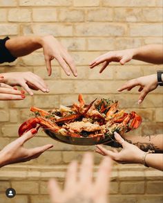 several people reaching for food in a bowl with lobsters on it and their hands above them